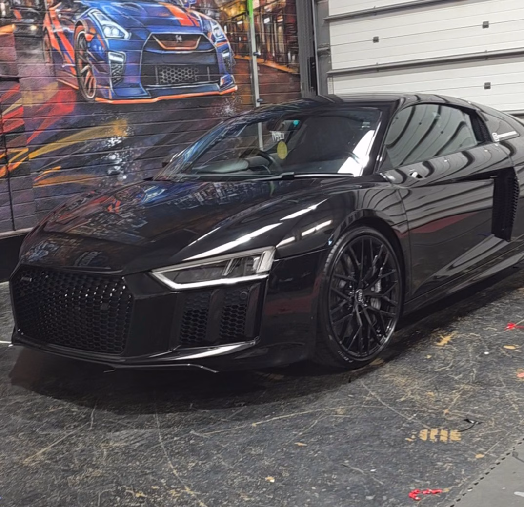 Glossy black Audi R8 sports car parked indoors with reflective detailing and mural of a blue and orange car on wall behind