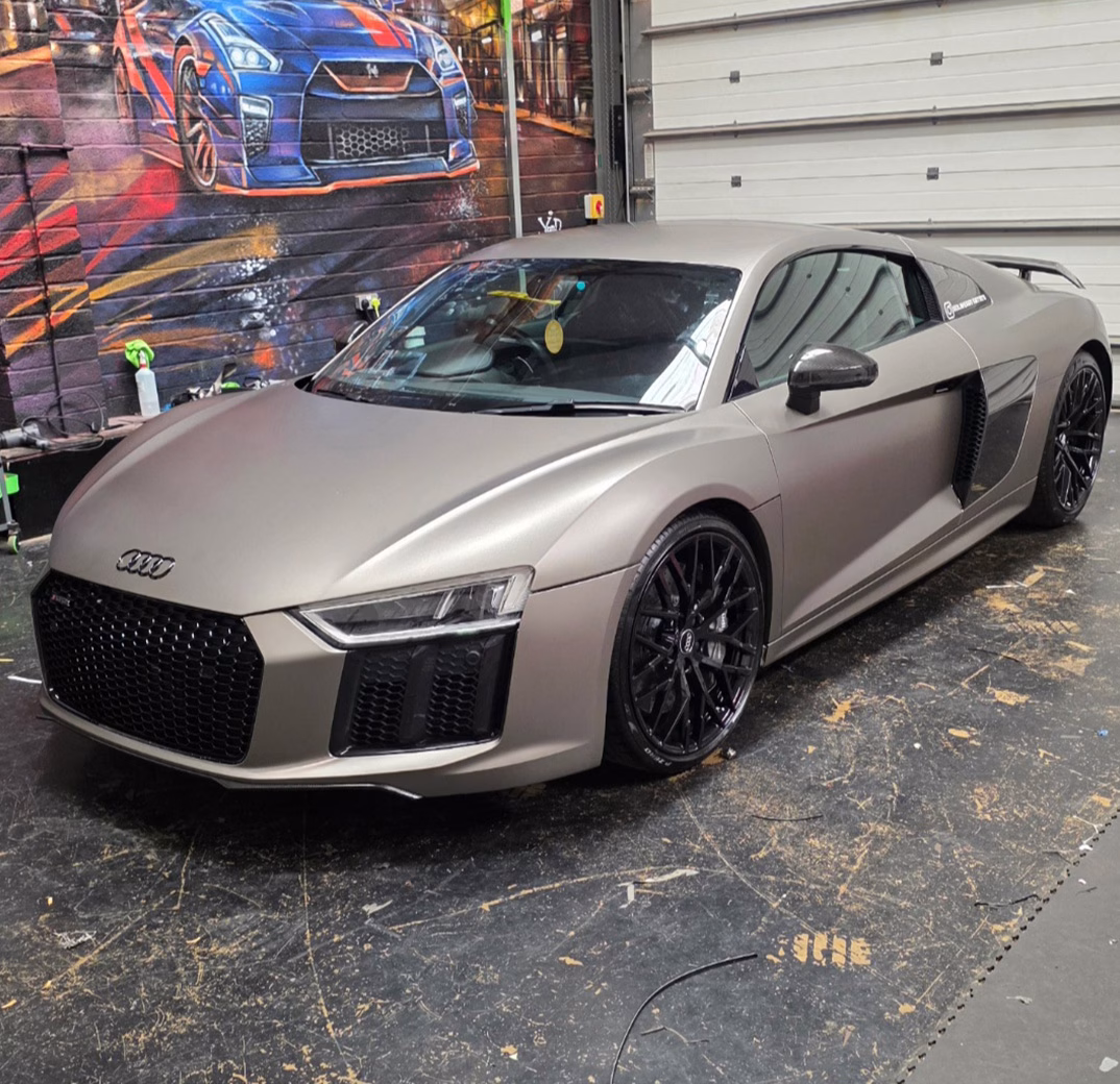 Matte grey Audi R8 sports car with black wheels inside a garage featuring a street art mural on the wall