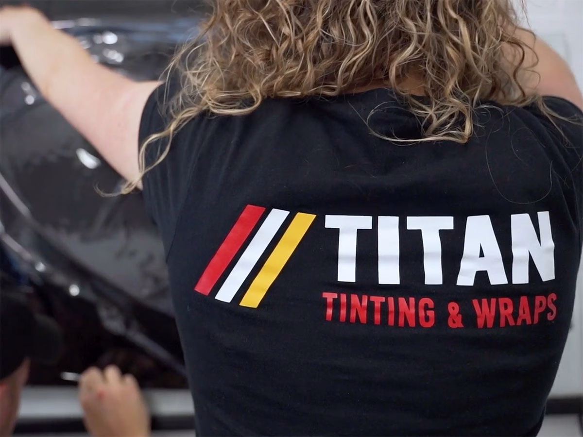 Person wearing a black shirt with the Titan Tinting & Wraps logo, working on a car wrap application